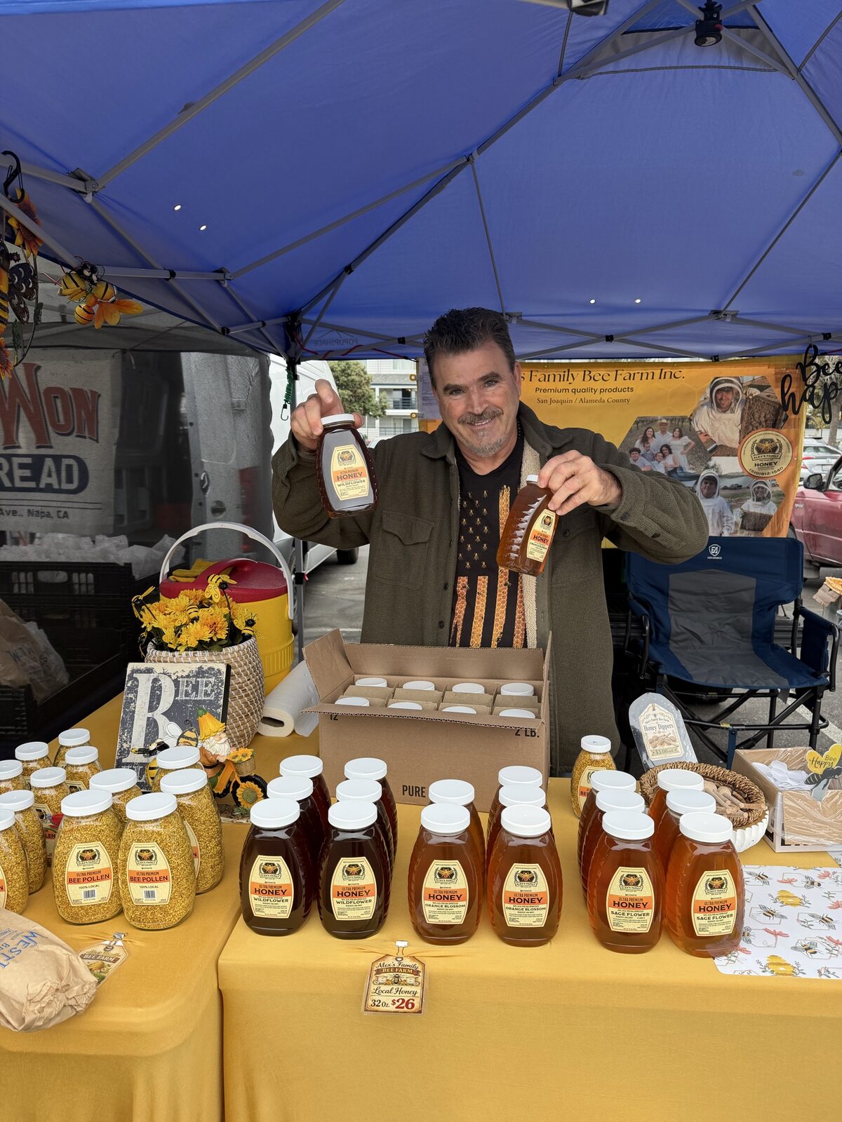 Alex of Alex&rsquo;s Family Bee Farm holding up jars of honey at the farmers market